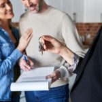 A real estate agent handing keys to a new homeowner with documents on a table