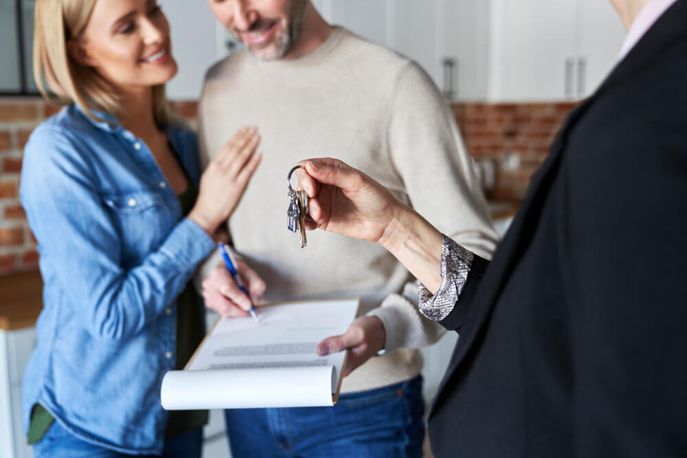 A real estate agent handing keys to a new homeowner with documents on a table